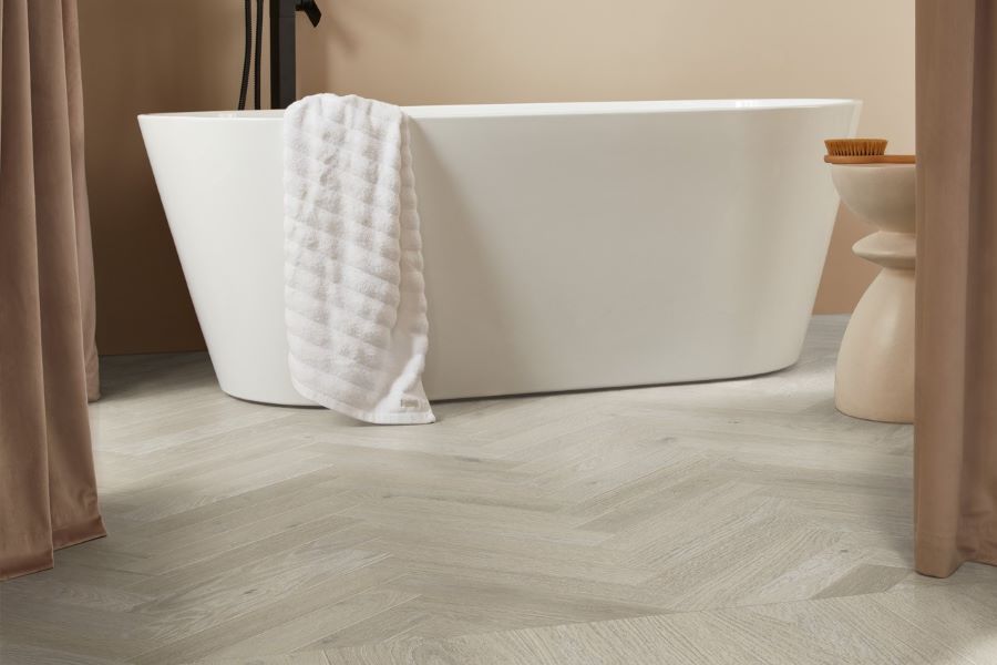 light brown luxury vinyl wood effect herringbone flooring in a bathroom with a white freestanding bath